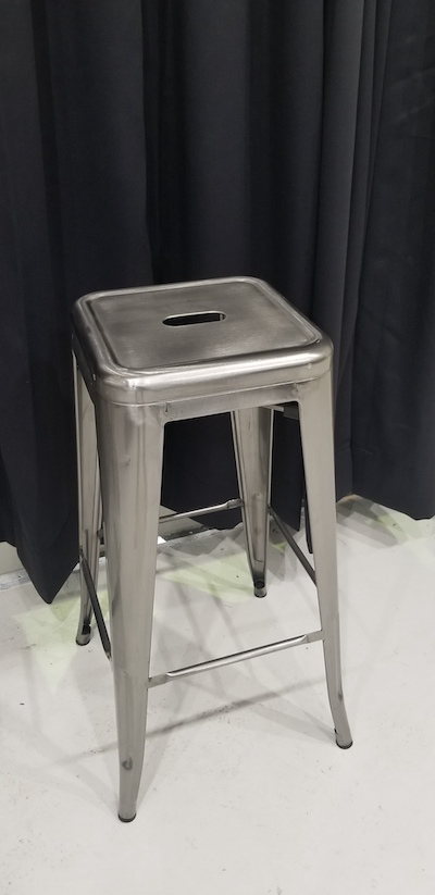 Silver industrial looking bar stool, it is backless, 4 legs, seat  which is padless and has small cut-out  
