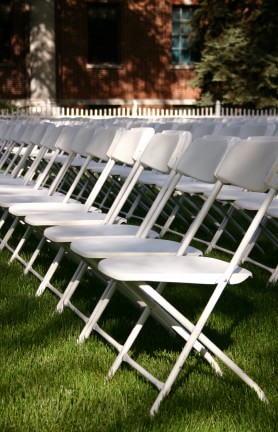 white plastic with metal folding chairs set up in rows on grass for outdoor event