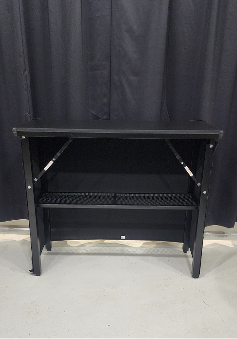 back of portable bar, black top, open back with shelf with black drape in background on concrete floor