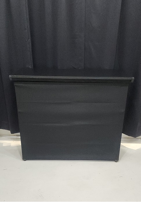 front of portable bar, black top, black skirt with black drape in background on concrete floor